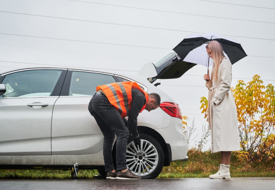 voiture grise arrêtée, homme en gilet orange changeant le pneu